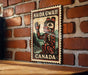 A metal sign with a red and black design hangs on a brick wall, featuring a depiction of a Native American symbol and the text "HAIDA GWALL CANADA".