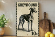 A greyhound dog illustration on a 10 cent postage stamp, placed on a wooden surface next to a wooden cutting board and some lemons.