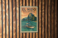 A vintage-style poster of El Nido, a popular tourist destination in the Philippines, is displayed on a wooden wall.