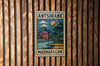 a vintage-style stamp or sign with a tropical landscape, including a house, tree, and body of water, hanging on a wooden wall.
