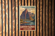 A vintage postage stamp featuring a mountain landscape with a small cabin, hanging on a wooden wall.