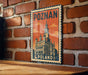 A vintage-style metal sign with the text "POZNAN POLAND" and an illustration of a castle-like building, mounted on a brick wall.