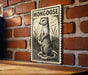 a wooden table with a framed illustration of a mongoose on it, mounted on a brick wall.