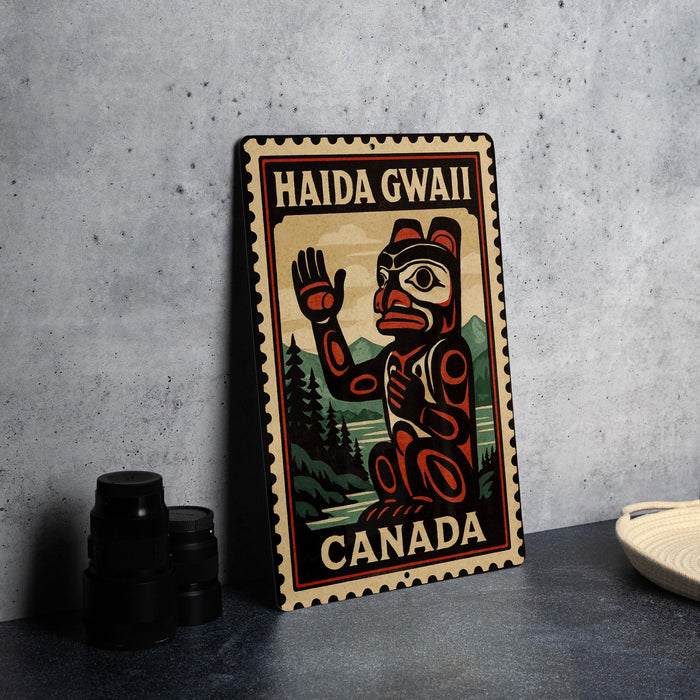 A metal sign with a stamp-like design, featuring a stylized illustration of a bear and the text "HAIDA GWAII CANADA" on it, is displayed on a table.