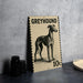 A greyhound dog illustration on a postage stamp-like frame, placed on a countertop next to some black camera lenses.