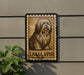 a large brown and black dog sitting on a wall, with a stamp-like border around it.