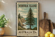 A vintage postage stamp from Norfolk Island, featuring a pine tree and a coastal landscape, is displayed on a shelf next to a wooden cutting board and a potted plant.