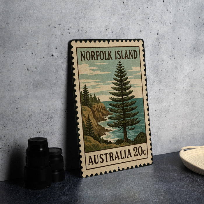 A vintage postage stamp from Norfolk Island, featuring a pine tree and a coastal landscape, is displayed on a table.