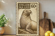 a framed stamp-like artwork depicting a sea lion, with a price tag of 60 cents. The artwork is displayed on a shelf next to a wooden cutting board and a potted plant.
