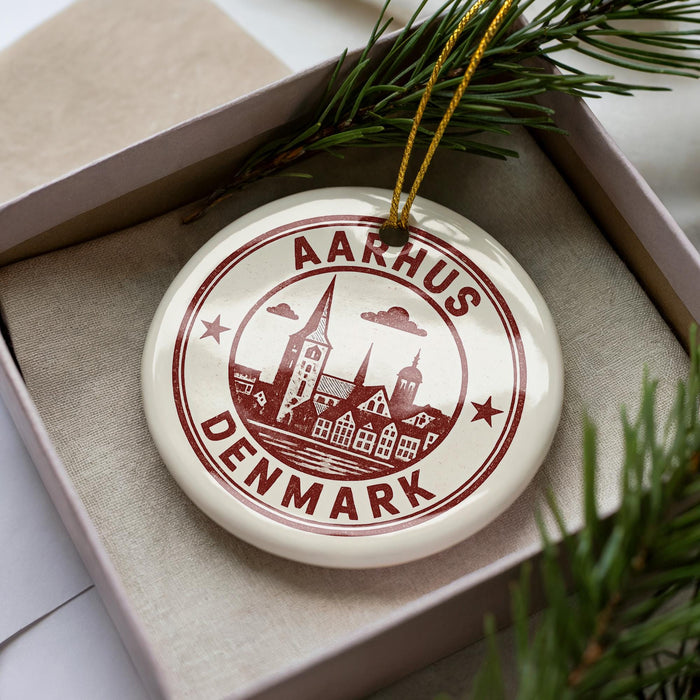 A decorative ornament with the text "AARHUS DENMARK" printed on it, placed inside a box with pine branches.