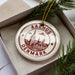 A decorative ornament with the text "AARHUS DENMARK" printed on it, placed inside a box with pine branches.