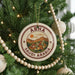 A round ornament on a Christmas tree, featuring a design of a cityscape with buildings and mountains, along with the text "ABHA SAUDI ARABIA".