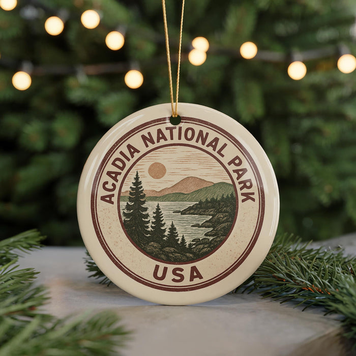 A circular ornament with the text "ACADIA NATIONAL PARK USA" and a scenic landscape design, hanging from a string.