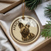A circular ornament with a picture of a wild dog on it, placed in a box with pine branches.