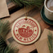 A circular ornament with the text "ALBUQUERQUE NEW MEXICO" is displayed on a wooden surface, surrounded by pine branches and a cup of coffee.