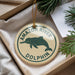A round ornament with a green dolphin and the text "AMAZON RIVER DOLPHIN" is displayed in a box, surrounded by pine branches.