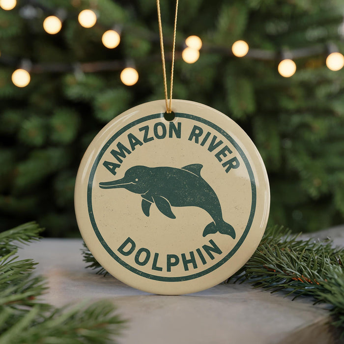 A round ornament with the text "AMAZON RIVER DOLPHIN" and a graphic of a dolphin is displayed on a table, with a blurred background of a Christmas tree.