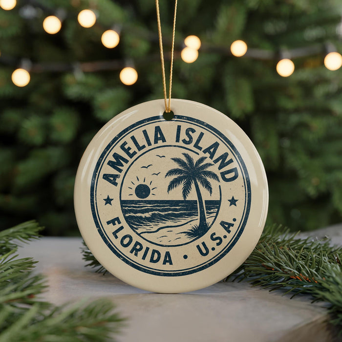 A circular ornament with a palm tree and beach scene, surrounded by a string of lights, placed on a surface with pine branches.