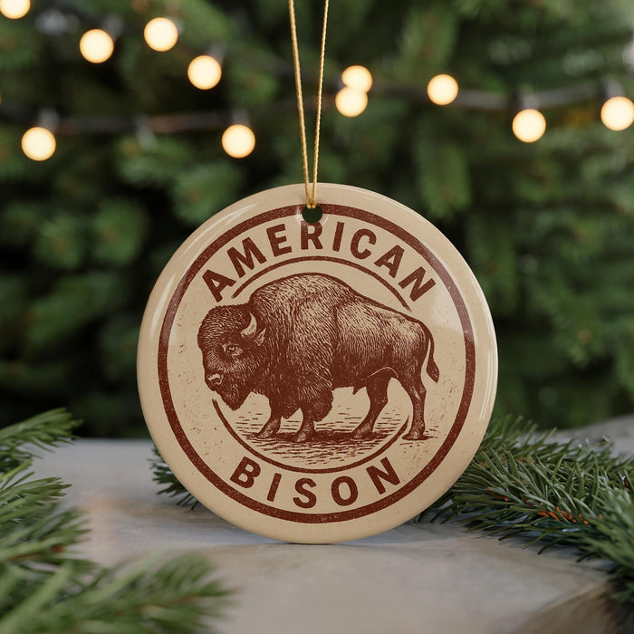 A circular ornament featuring a bison illustration, with the text "AMERICAN BISON" printed on it, is displayed in front of a blurred background of Christmas lights.