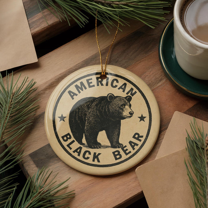 A circular ornament featuring a black bear, with the text "AMERICAN BLACK BEAR" printed on it, is displayed on a wooden surface alongside a cup of coffee and some pine branches.