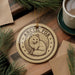 a circular ornament with a drawing of an Arctic fox, surrounded by stars, placed on a wooden surface.