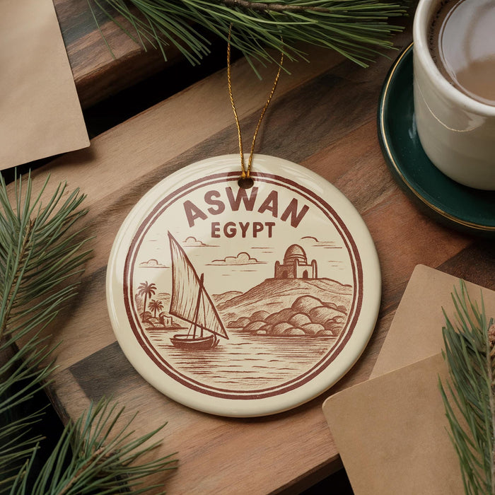 A circular ornament with a sailboat and a castle in the background, surrounded by pine branches and a cup of coffee on a wooden surface.