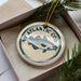 A decorative ornament in a box, featuring a blue and white design of a fish and the text "ATLANTIC COD".