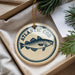 A circular ornament with the text "ATLANTIC COD" and a fish illustration is displayed in a box with pine branches.