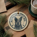 A circular ornament featuring an image of an Australian Cattle Dog, with the text "AUSTRALIAN CATTLE DOG" printed on it. The ornament is hanging from a string, and there is a cup of coffee and some pine branches in the background.