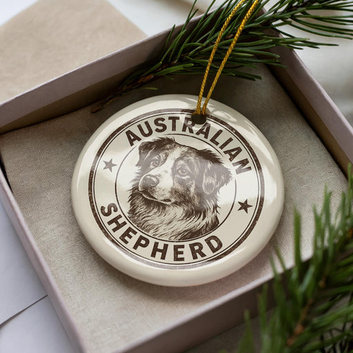 A circular ornament with the text "AUSTRALIAN SHEPHERD" and an image of a dog's head is displayed in a box, surrounded by pine branches.