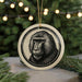 A circular ornament featuring a detailed illustration of a monkey's face, surrounded by a decorative border, is displayed in front of a blurred background of Christmas lights.