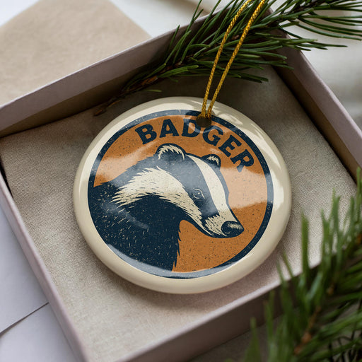 A circular ornament with a badger image and the word "BADGER" written on it, placed inside a box with pine branches.