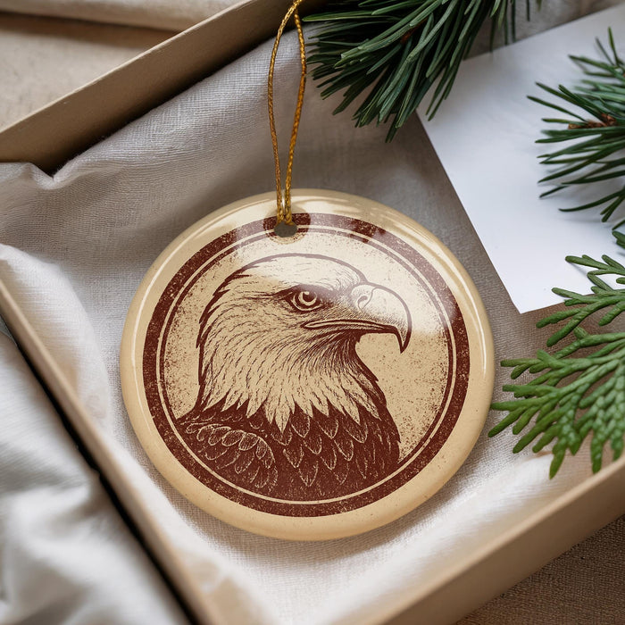 A circular ornament featuring an eagle's head is displayed in a box, surrounded by pine branches.