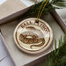 A round ornament with a snake design, featuring the text "BALL PYTHON" on it, is displayed in a box with pine branches.