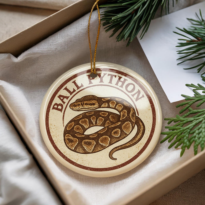 A round ornament with a snake design, hanging from a string, placed on a surface with pine branches.