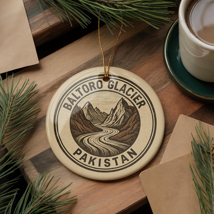 A circular ornament with the text "BALTORO GLACIER PAKISTAN" and a mountain landscape design hangs on a wooden surface, surrounded by pine branches and a cup of coffee.