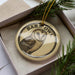 A circular ornament with a picture of an owl and the text "BARN Owl" on it, placed in a box with pine branches.