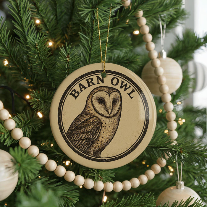A round ornament with a barn owl design hangs on a Christmas tree, surrounded by other ornaments and lights.