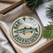 A circular ornament with the text "BARRACUDA" and an illustration of a fish is displayed in a box with pine branches.