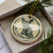A circular ornament with a bat-eared fox illustration and the text "BAT-EARED FOX" printed on it, placed inside a box with pine branches.
