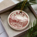 A circular ornament with the text "BATH ENGLAND" printed on it, surrounded by pine branches.