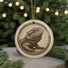 A ceramic ornament featuring a detailed illustration of a bearded dragon is displayed in front of a blurred background of Christmas lights.
