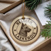 A circular ornament with a dog image and the text "Belgian Laekenois" printed on it, placed in a box with pine branches.