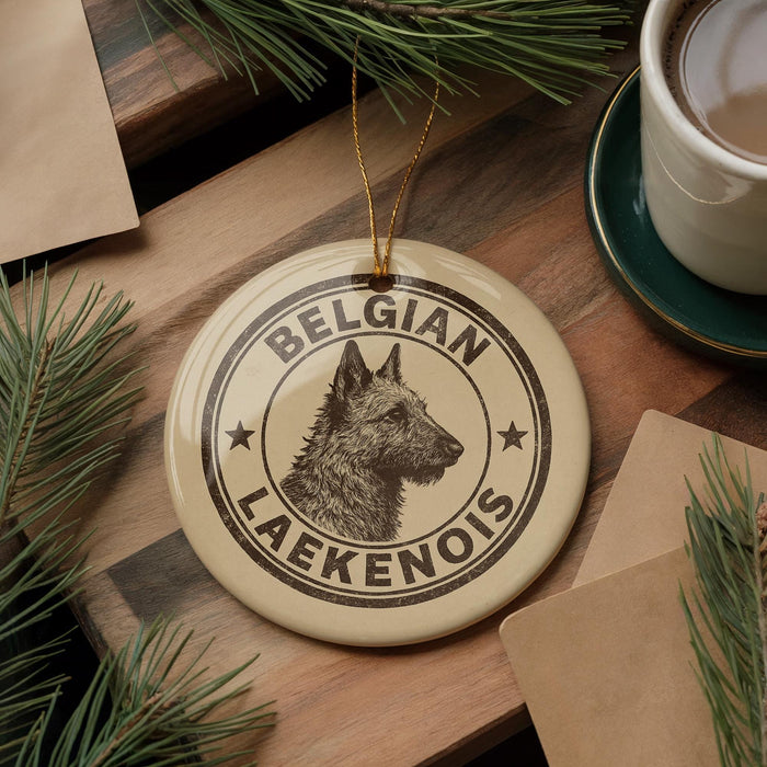 A round ornament with a dog's head and the text "BELGIAN LAEKENOIS" is displayed on a wooden surface, surrounded by pine branches and a cup of coffee.