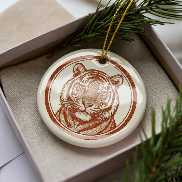 A ceramic ornament in the shape of a tiger's head, with a brown and white color scheme, is displayed in a box surrounded by pine branches.