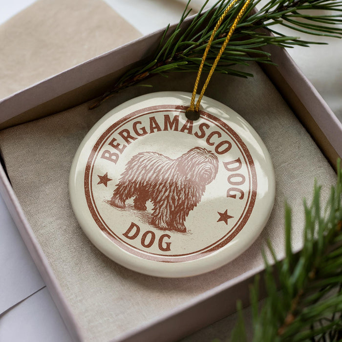 A round ornament with the text "BERGAMASCO DOG" and an illustration of a shaggy dog is displayed in a box, surrounded by pine branches.
