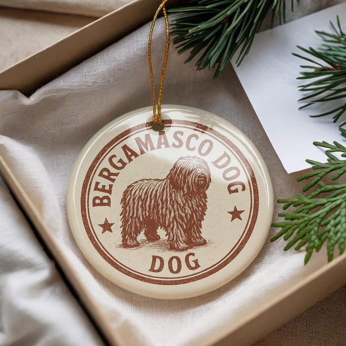 A round ornament with a brown and white design featuring a shaggy dog, placed in a box with pine branches.