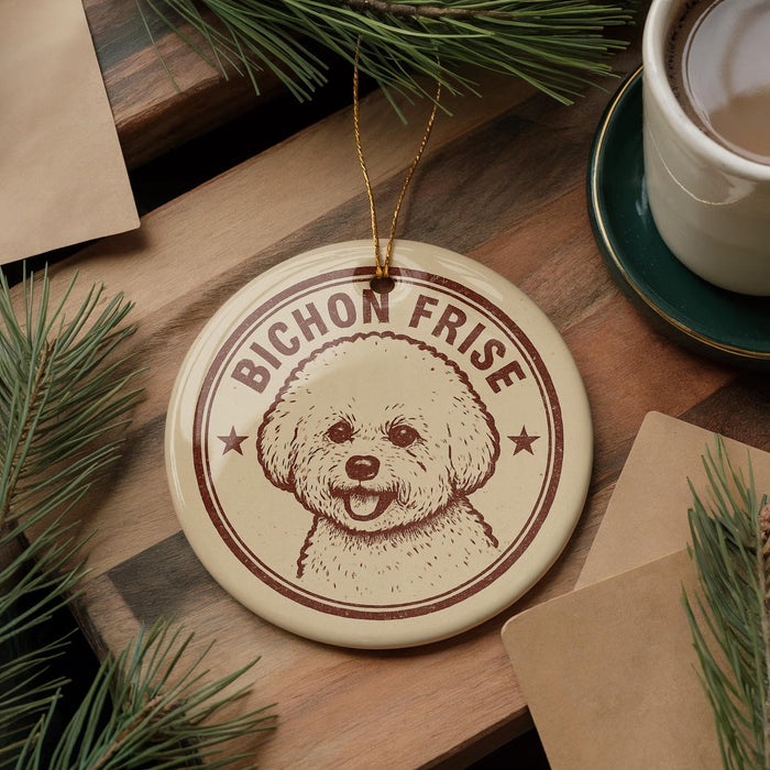 A round ornament featuring a poodle's face with the text "BICHON FRISE" is displayed on a wooden surface, surrounded by pine branches and a cup of coffee.