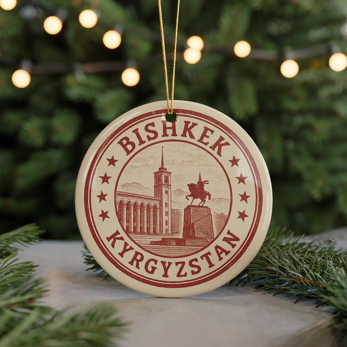 A circular ornament with the text "BISHKÉK Kyrgyzstan" and an illustration of a building and a statue, hanging from a string.