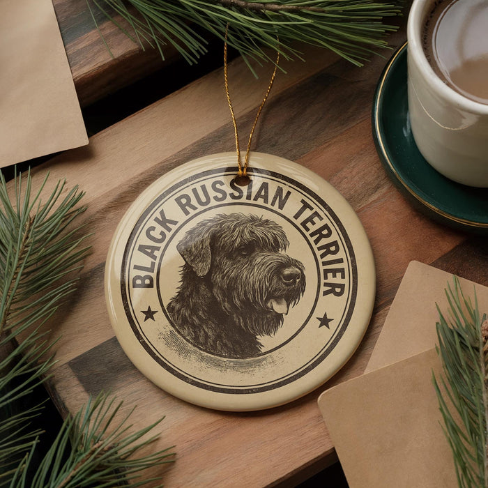 A circular ornament featuring a black Russian terrier dog's head, with the text "BLACK RUSSIAN TERRIER" printed on it, is displayed on a wooden surface alongside a cup of coffee and pine branches.